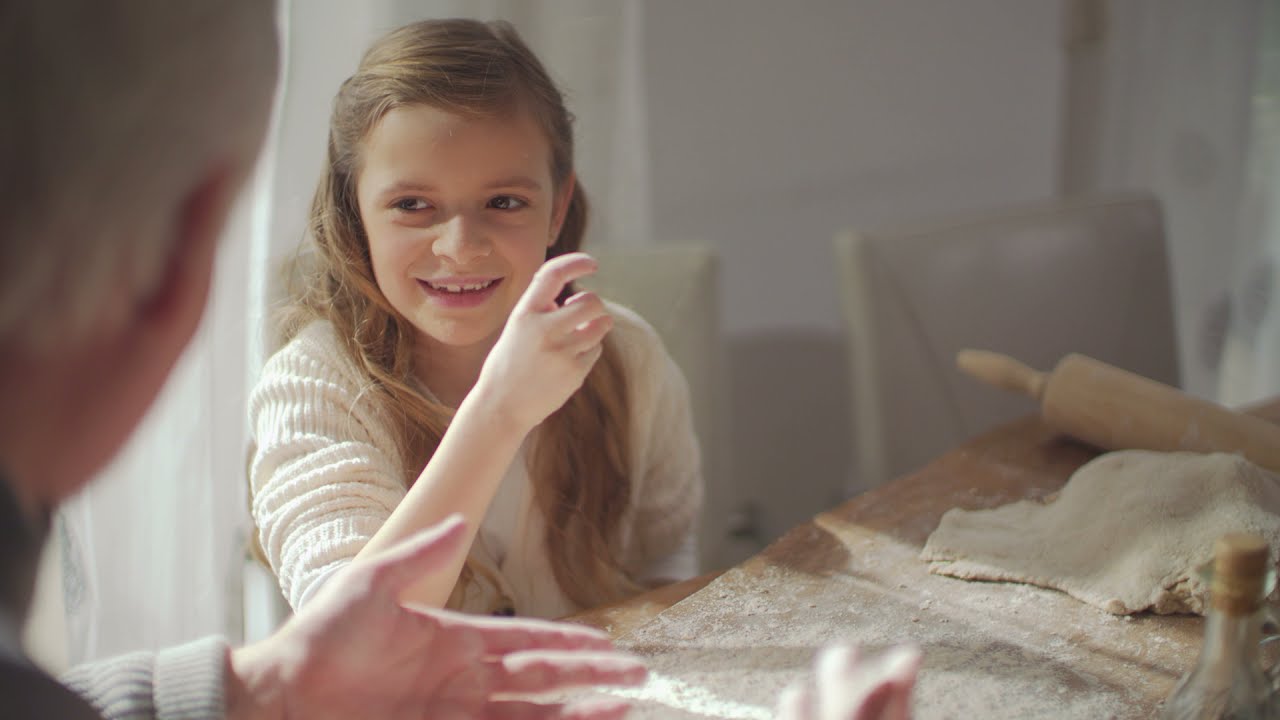 Girl with grandfather with kneaded dough on table